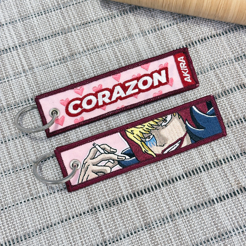 Double-sided embroidered keychain of Donquixote Rosinante (Corazón) from One Piece. One side features the word "CORAZON" with pink hearts, and the other side shows Rosinante holding a cigarette
