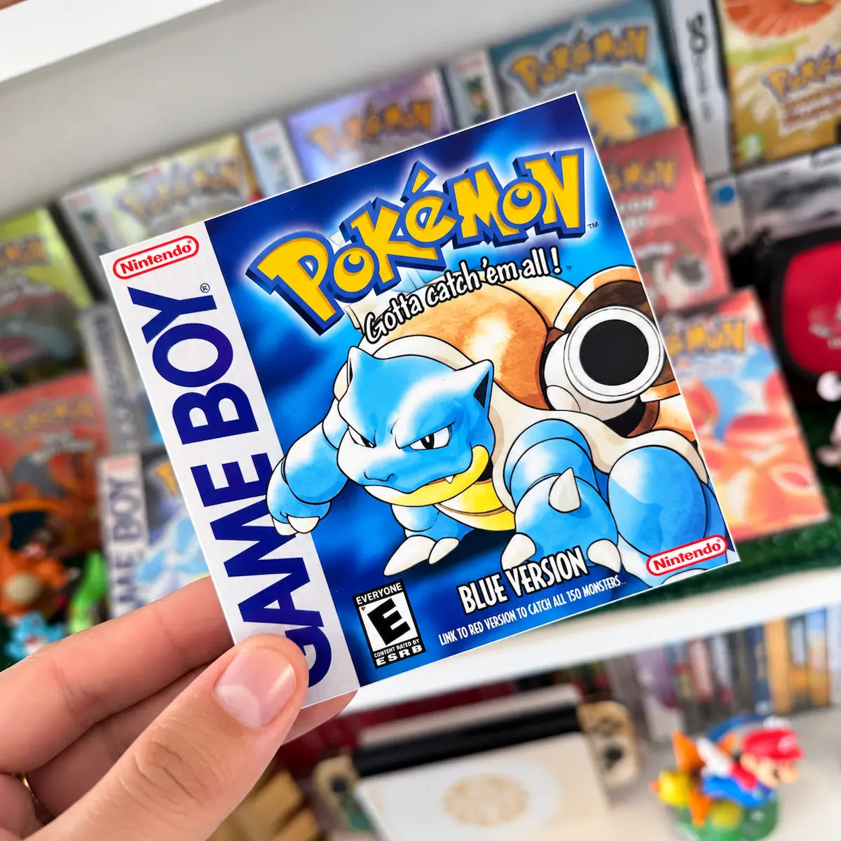 Pokémon Blue Version sticker with Blastoise held in front of a retro Pokémon game collection