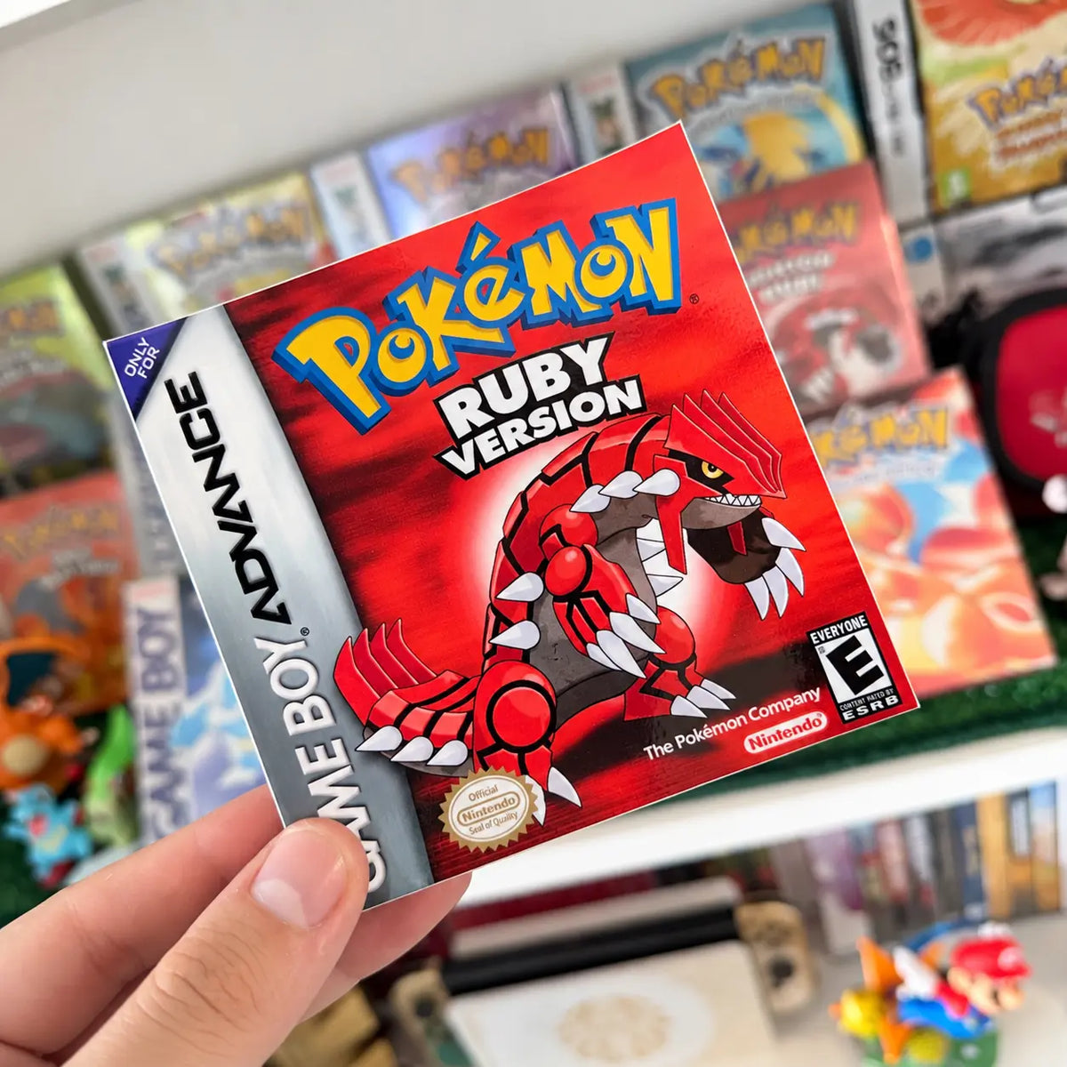 Pokémon Ruby Version sticker with Groudon held in front of a retro Pokémon game collection