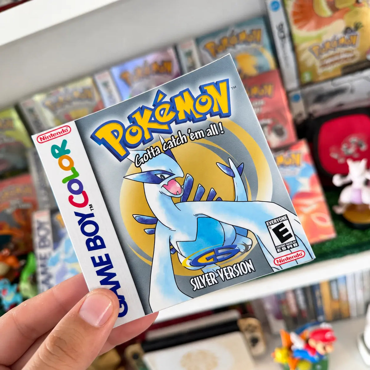 Pokémon Silver Version sticker with Lugia held in front of a retro Pokémon game collection