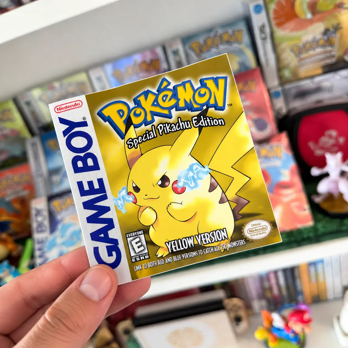Pokémon Yellow Version sticker with Pikachu held in front of a retro Pokémon game collection